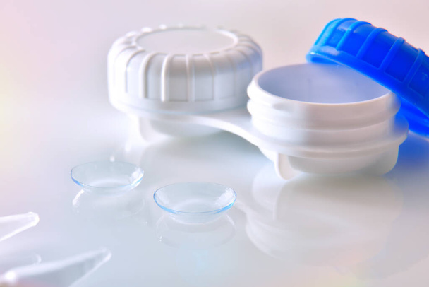 Contact lenses and case reflected on white glass table - Foto, afbeelding