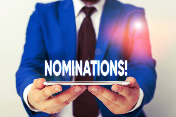 Handwriting text writing Nominations. Concept meaning action of nominating or state being nominated for prize Businessman in blue suite with a tie holds lap top in hands. - Photo, Image