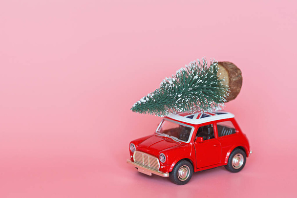 Coche de juguete rojo con un árbol de Navidad en el techo sobre fondo de papel rosa. Entrega de invierno, Navidad, feliz año nuevo 2020 concepto de celebración. tarjeta de felicitación, maqueta, espacio para copiar, lugar para el texto, plantilla
 - Foto, imagen