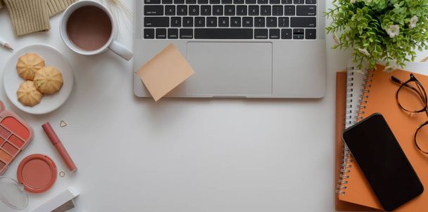Cálido espacio de trabajo femenino beige con computadora portátil, maquillaje y suministros de oficina
  - Foto, imagen