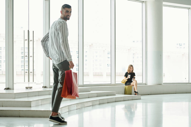 attraktive junge Frau ruht sich nach dem Einkauf aus, ihr Freund mit Einkaufstasche läuft zu ihr - Foto, Bild