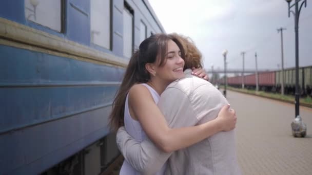 радісна красива дівчина обіймає хлопця і сміється біля вагона поїзда на залізничній платформі після розлуки
 - Кадри, відео