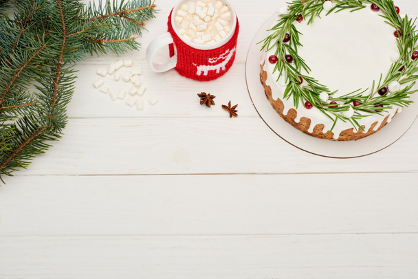 bovenaanzicht van kersttaart op witte houten tafel met kopje cacao met marshmallows en sparren takken - Foto, afbeelding