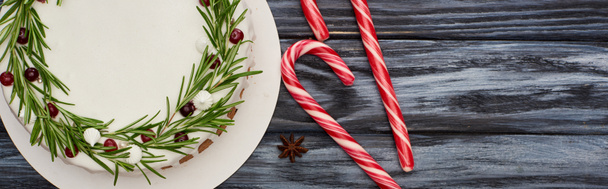 vrchní pohled na vánoční koláč s rozmarýnem a brusinkami na tmavém dřevěném stole s candy canes - Fotografie, Obrázek