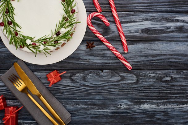 vista superior del pastel de Navidad con romero y arándanos, bastones de caramelo, tenedor y cuchillo en la servilleta en la mesa de madera oscura
  - Foto, imagen