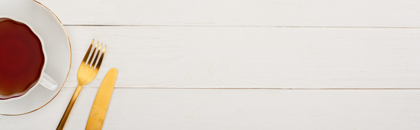 πάνω όψη του φλιτζανιού του τσαγιού, πιρούνι και μαχαίρι σε λευκό ξύλινο τραπέζι - Φωτογραφία, εικόνα