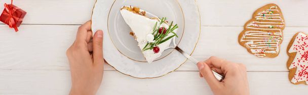 przycięty widok kobiety z kawałkiem ciasta świątecznego i ciasteczek na białym drewnianym stole - Zdjęcie, obraz