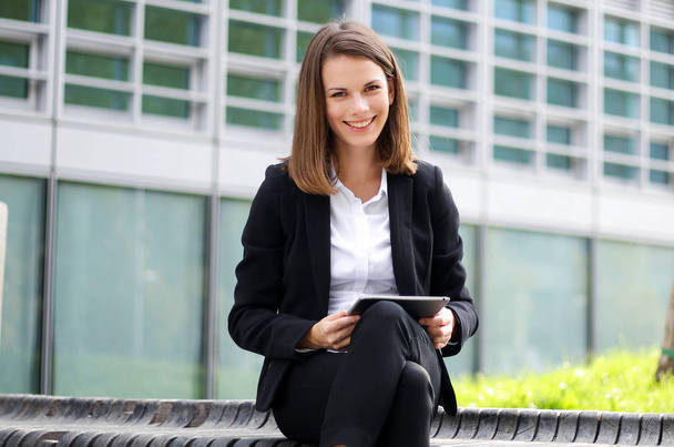Smiling businesswoman using a digital tablet outdoor sitting on a bench - Photo, Image