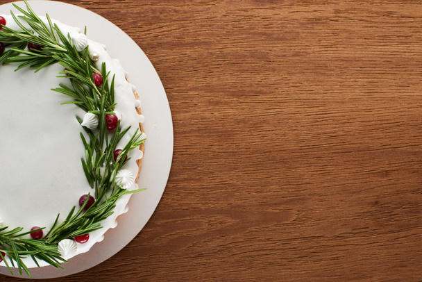 pohled na tradiční vánoční koláč s polevou, rozmarýnem a brusinkami na dřevěném stole  - Fotografie, Obrázek