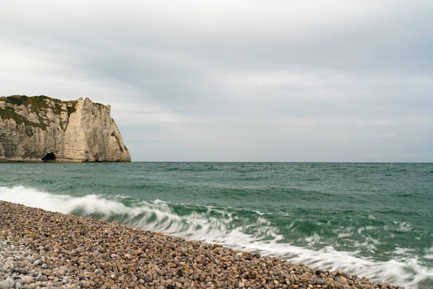 хвилі падають на скелю і гальковий пляж з зубчастими скелями на фоні
 - Фото, зображення