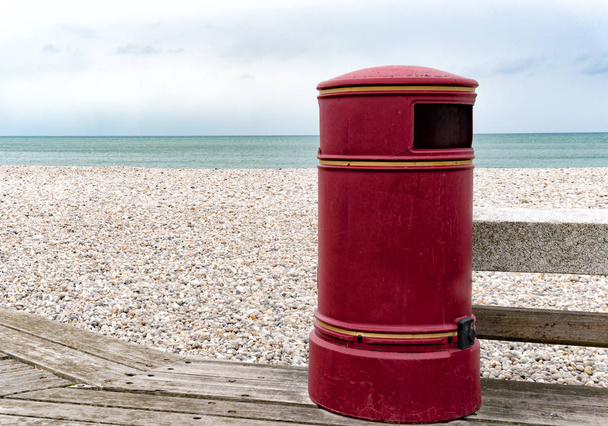 duży zabytkowy czerwony kosz na śmieci na drewnianej promenadzie na skalistej plaży - Zdjęcie, obraz