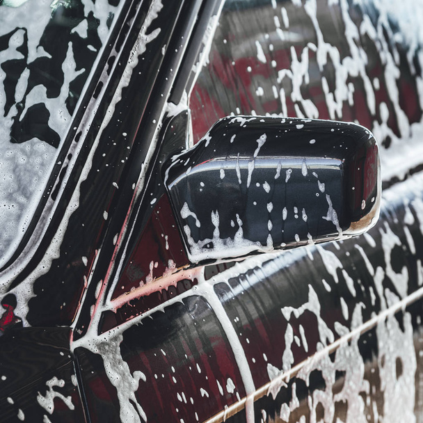 Car covered in white foam during cleaning, carwash washing process, car in soup - Foto, Imagem