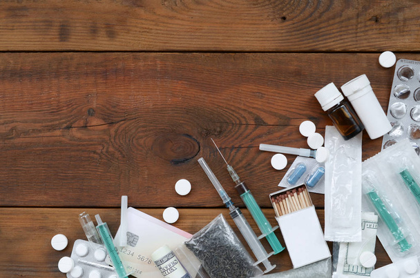 Багато наркотичних речовин і пристроїв для приготування ліків лежать на старому дерев'яному столі
 - Фото, зображення