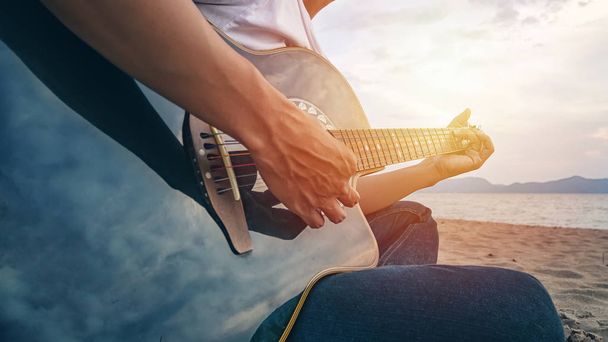 man's hands playing acoustic guitar, capture chords by finger on sandy beach at sunset time. playing music concept - Photo, image
