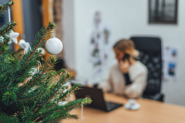 Weihnachtsbaum im Büro geschmückt, Geschäftsfrau im unscharfen Hintergrund arbeitet am Laptop - Foto, Bild