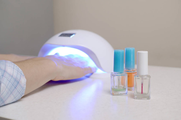 Trzy bezbarwne przezroczyste lakieru do paznokci butelki w tle żeńskich rąk w żelu uv led lampy do suszenia manicure - Zdjęcie, obraz