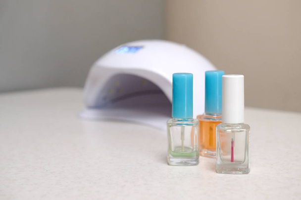 Luzes de lâmpada de diodo UV para unhas e conjunto de esmalte de unhas cosméticas para manicure e pedicure no fundo da mesa branca
 - Foto, Imagem
