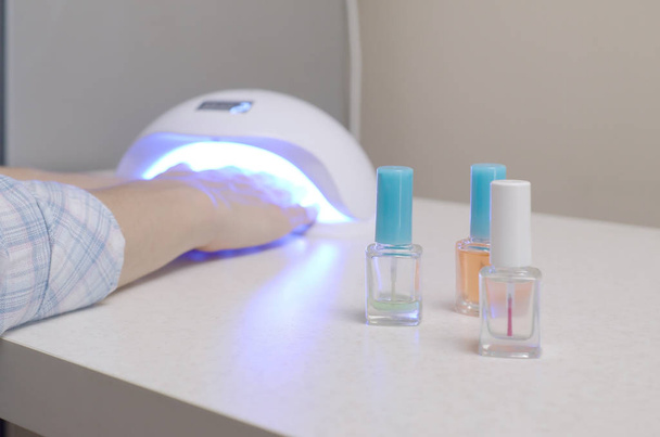 Drie kleurloze transparante nagellak flessen in de achtergrond van vrouwelijke handen in gel uv led nagel witte lamp voor het drogen manicure - Foto, afbeelding