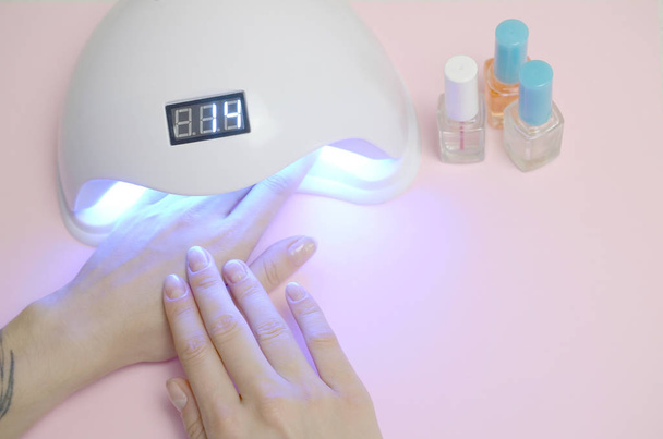 Hands of young woman at manicure procedure close up on pastel pink background - Photo, Image