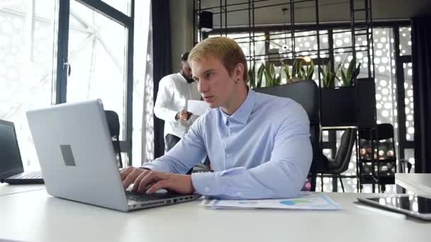 Gros plan d'un beau travailleur de bureau expérimenté de 30 ans tapant sur son ordinateur sur le lieu de travail dans un bureau moderne avec des collègues d'entreprise
 - Séquence, vidéo