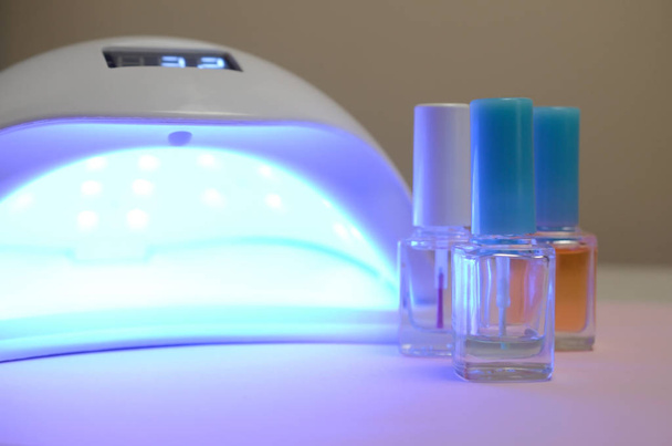 Luzes de lâmpada de diodo UV para unhas e conjunto de esmalte cosmético para manicure e pedicure em fundo pastel
 - Foto, Imagem