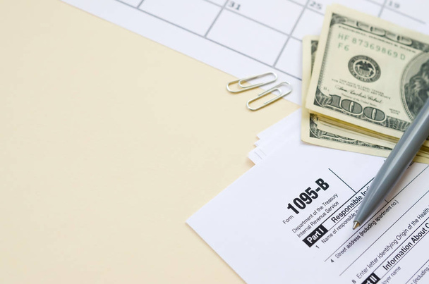 IRS Form 1095-B Health Coverage tax blank lies with pen and many hundred dollar bills on calendar page - Φωτογραφία, εικόνα