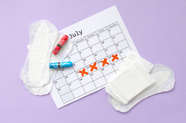 Almohadillas y tampones menstruales en el calendario del período de menstruación acostado plano sobre fondo lila
 - Foto, imagen