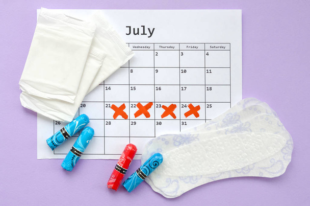Menstruatie kussens en tampons op menstruatie periode kalender plat lag op lila achtergrond - Foto, afbeelding