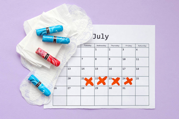 Menstrual pads and tampons on menstruation period calendar flat lay on lilac background - Photo, Image