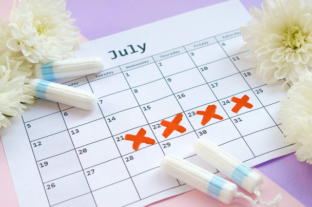 Menstrual tampons on menstruation period calendar with white flowers on lilac and pink background - Photo, Image