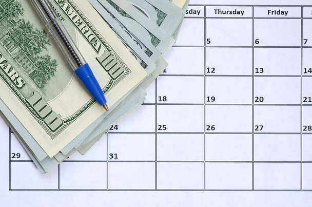 Pen and many hundred US dollar bills on calendar page close up - Foto, Imagem