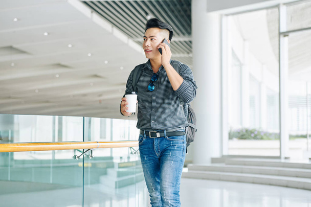 Mladý asijský muž chodí v kancelářské budově a mluví na hone  - Fotografie, Obrázek