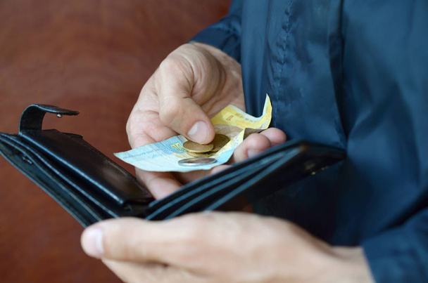 Ukrayna 'nın küçük banknotları ve eski siyah çantalı bozuk paraları olan bir erkek eli. - Fotoğraf, Görsel
