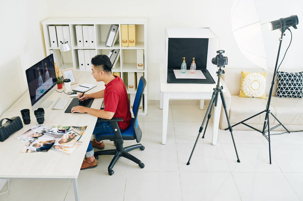 kreativer junger freischaffender vietnamesischer Designer arbeitet am Computer am Tisch in seinem Heimatatelier - Foto, Bild