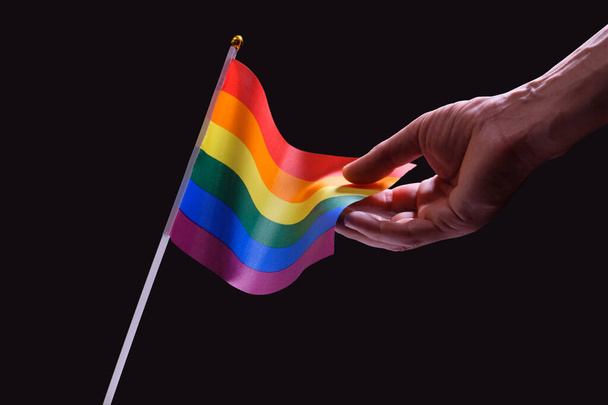 Male hand touches LGBT rainbow flag waving on a black background - Photo, Image