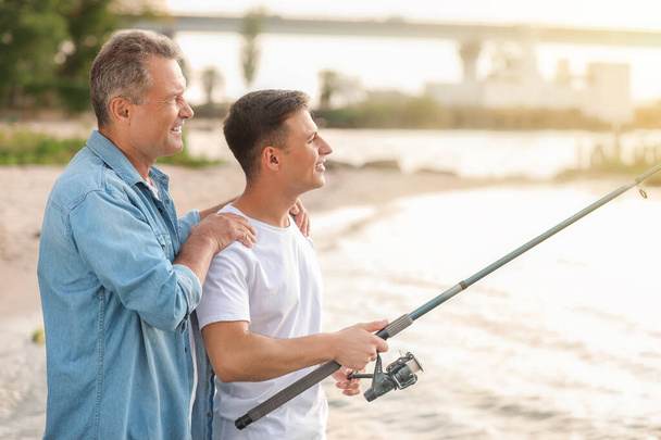 Jongeman en zijn vader vissen op de rivier - Foto, afbeelding