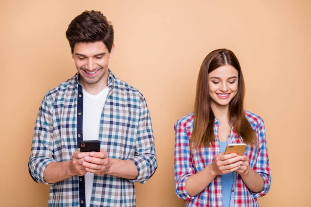 Portrait of his he her she nice attractive lovely focused concentrated addicted cheerful cheery couple wearing checked shirt using 5g app isolated over beige pastel color background - Fotó, kép