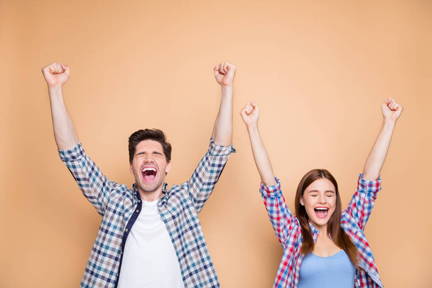 Portrait of his he her she nice attractive satisfied delighted cheerful cheery couple wearing checked shirt celebrating rising hands up good luck isolated over beige pastel color background - 写真・画像