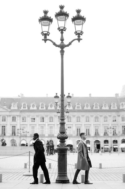 Czarno-białe zdjęcie afro amerykańskich i kaukaskich mężczyzn stojących w pobliżu latarni ulicznej w mieście. - Zdjęcie, obraz