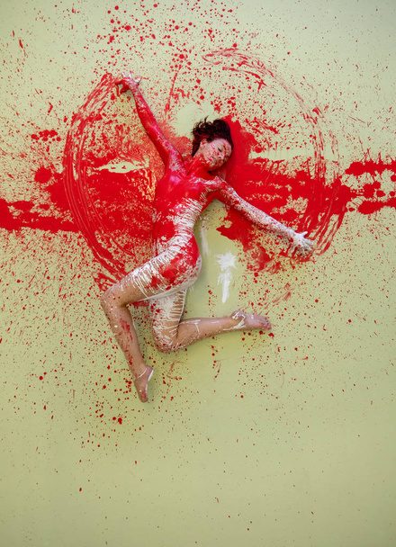 Νεαρή γυναίκα με κόκκινο χρώμα ζωγραφισμένη, ξαπλωμένη διακοσμητική, να χορεύει κομψά στο πάτωμα του στούντιο. Δημιουργική, εκφραστική σωματική τέχνη και ζωγραφική. - Φωτογραφία, εικόνα