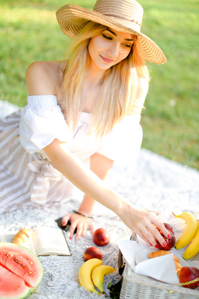 Молода жінка в капелюсі їсть фрукти і лежить на площині з книгою
. - Фото, зображення