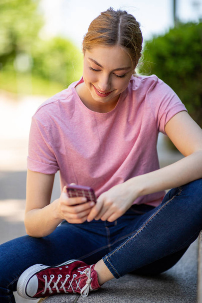 Retrato de una adolescente sonriente sentada afuera mirando el teléfono celular
  - Foto, Imagen