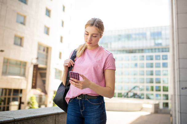 Porträt eines Teenagers, der mit Handy und Tasche durch die Stadt läuft - Foto, Bild