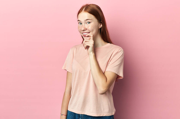 cheerful woman touching her lips while thinking, isolated pink studio background - Fotoğraf, Görsel