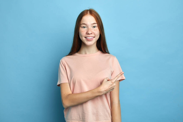 Smiling girl in T-shirt pointing finger away at copy space - Foto, Imagem