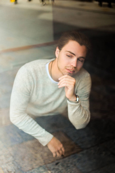 Fiatal ember ül, elmélkedés ablakban viselése szürke pulóver. - Fotó, kép