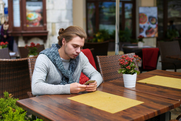Jeune homme assis au café sreet et bavarder par smartphone
. - Photo, image