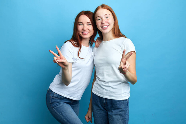 smiling good looking sisters in white t-shirts and jeans showing victory gesture - Фото, зображення