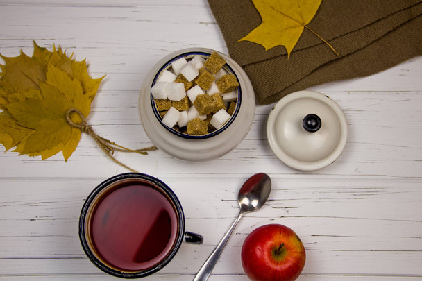 té en una taza blanca con azúcar blanca en cubos y azúcar de caña, hojas de arce y manzanas sobre un fondo claro de madera
. - Foto, imagen
