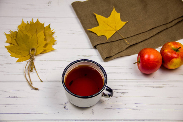 tè in una tazza bianca con zucchero bianco a cubetti e zucchero di canna, foglie d'acero e mele su uno sfondo di legno chiaro
. - Foto, immagini